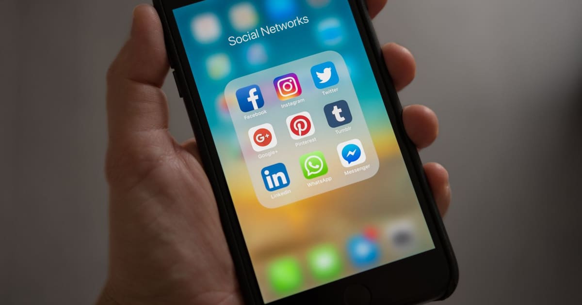 Mão segurando um celular com a pasta de redes sociais aberta, destacando o Instagram