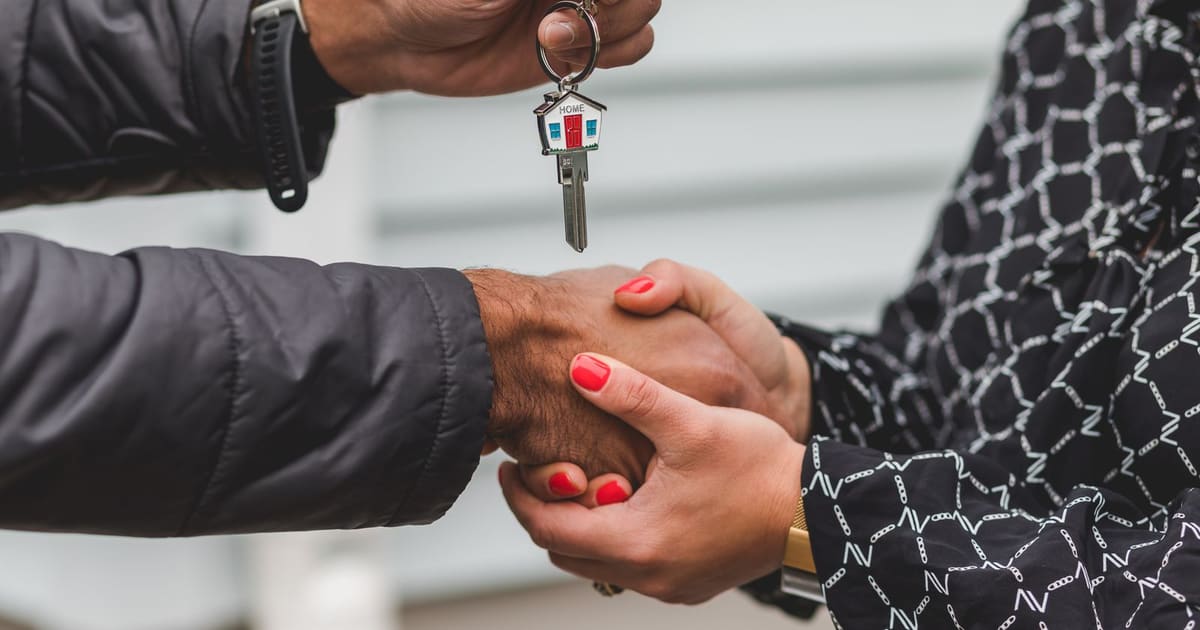 Corretor de imóveis entregando a chave da casa ao cliente durante um aperto de mãos
